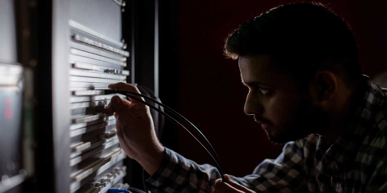 A photograph of a man inspecting a UTP cable on a server rack.